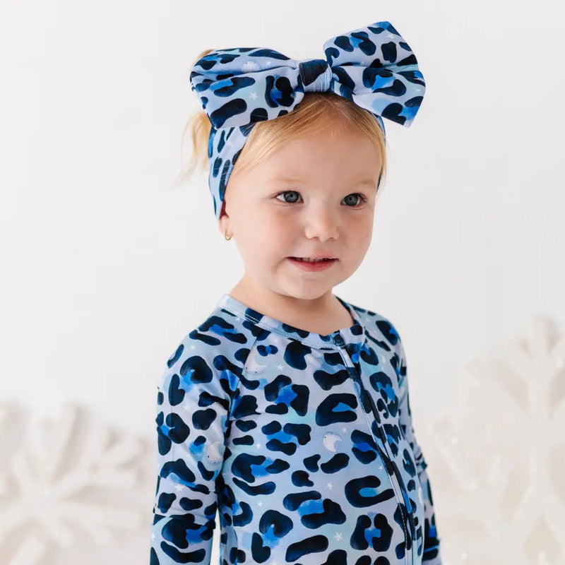 Child wearing a blue leopard print outfit and headband against a white background