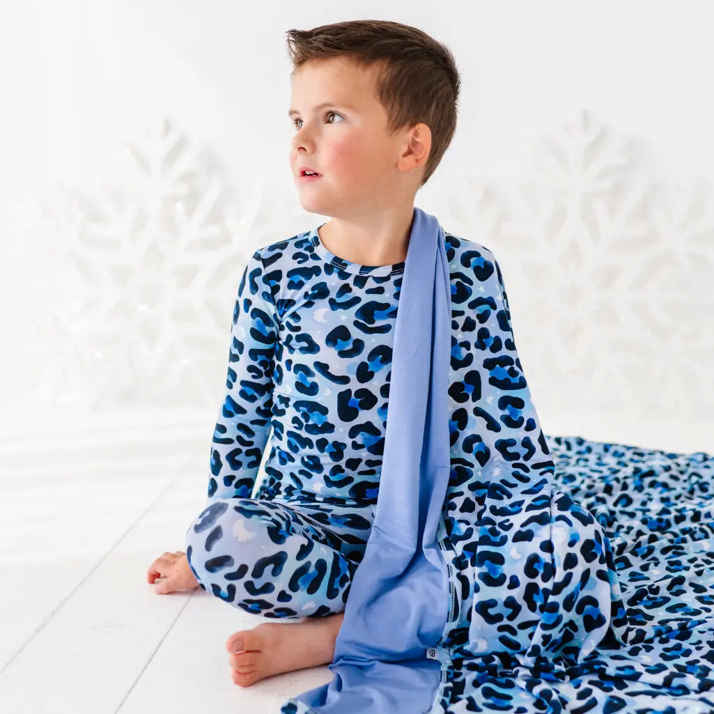 Child wearing blue leopard print pajamas with a matching blanket on a white background