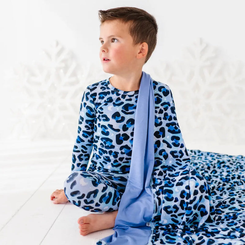 Child wearing blue leopard print pajamas with a matching blanket on a white background