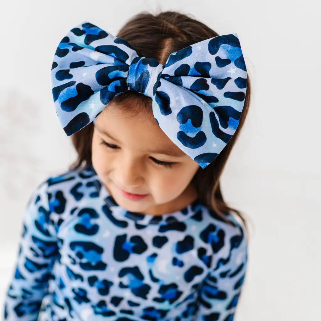 Child wearing a blue and black leopard print headband and outfit against a white background