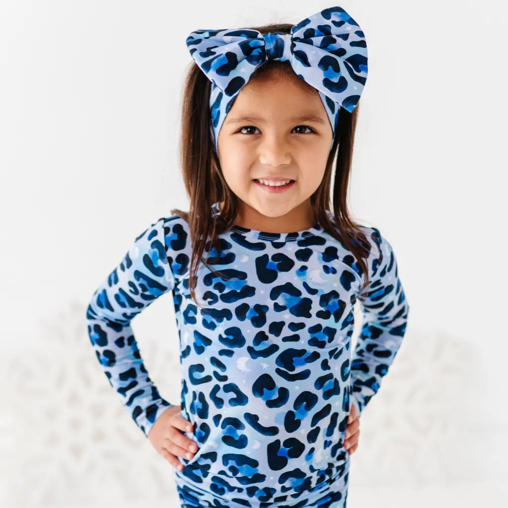 Child wearing a blue leopard print outfit with matching headband on a white background
