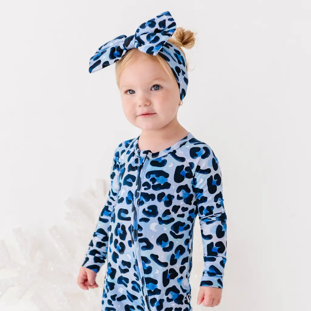 Baby wearing a blue leopard print onesie and headband on a white background