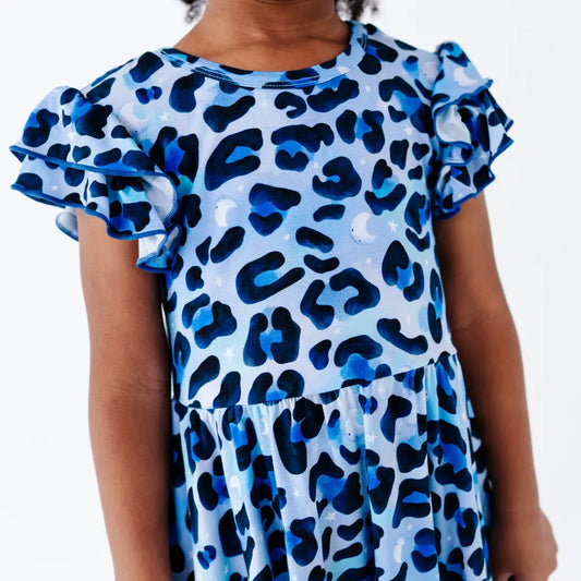 Young girl wearing a blue leopard-print ruffle-sleeve dress with stars and moons, on a white background