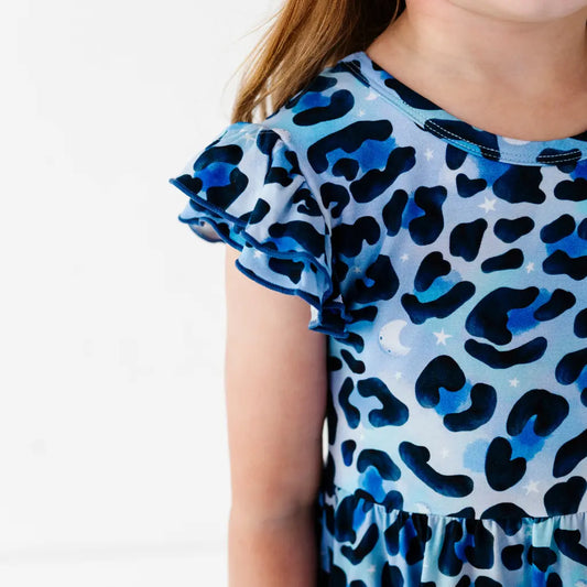 Close-up of a child wearing a blue leopard-print ruffle-sleeve dress with stars and moons, on a white background