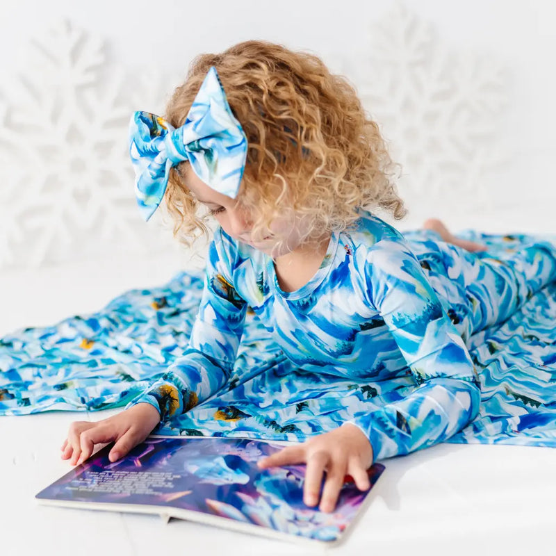 Child wearing a blue and white patterned outfit, sitting on a white surface with a book.