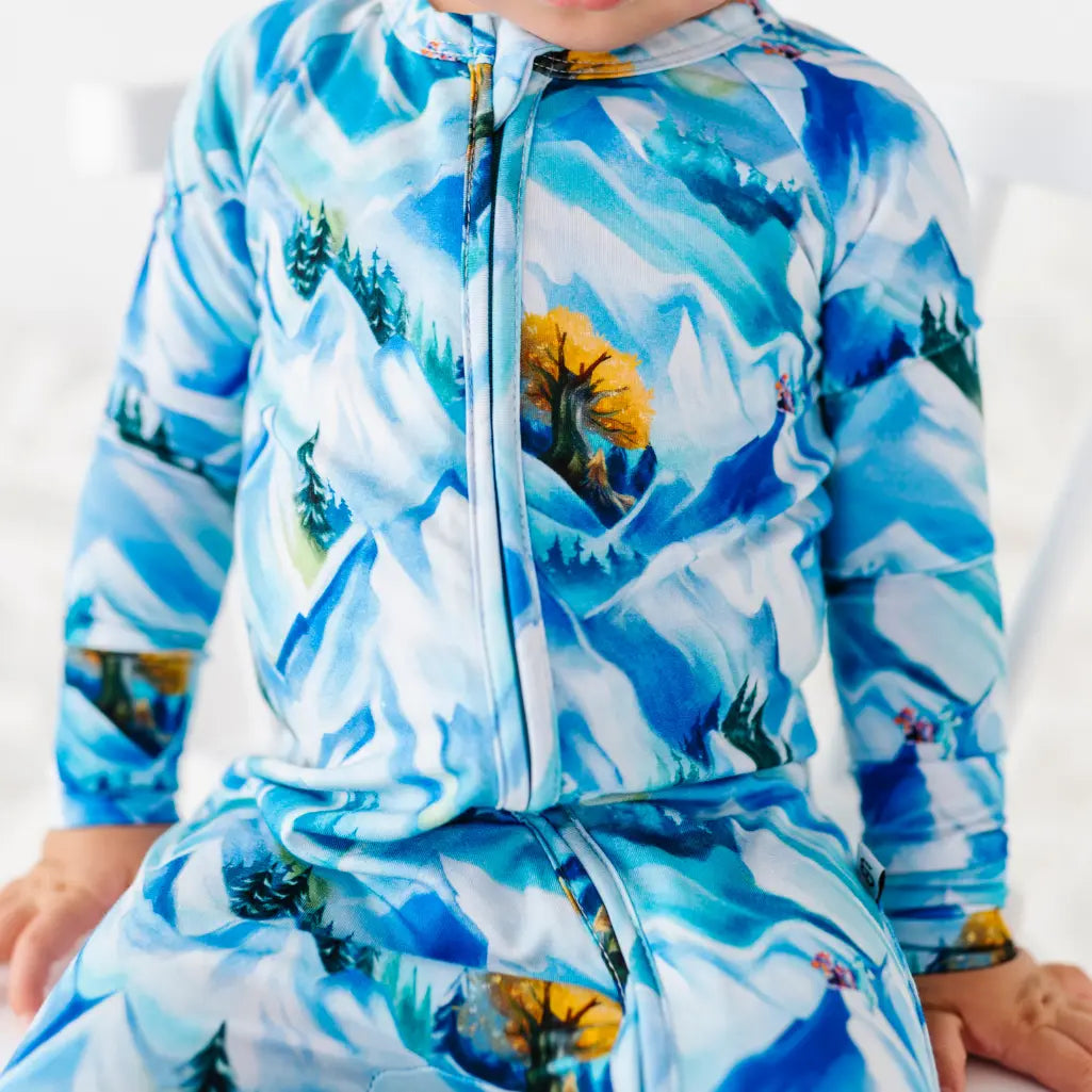 Child wearing a blue mountain-themed onesie with a white background