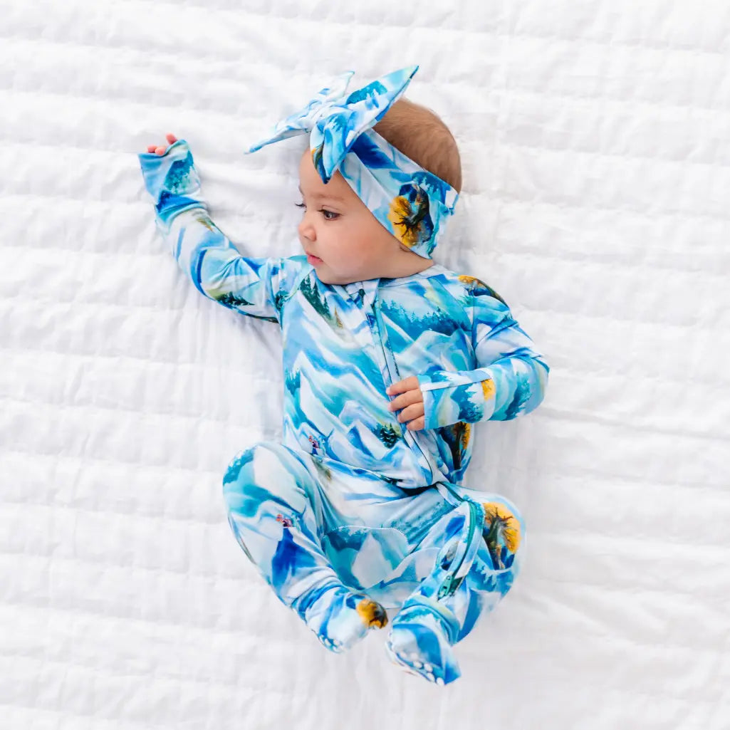 Baby wearing a blue and white patterned outfit and headband on a white textured surface
