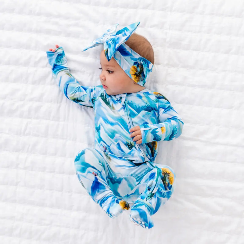 Baby wearing a blue and white patterned outfit and headband on a white textured surface
