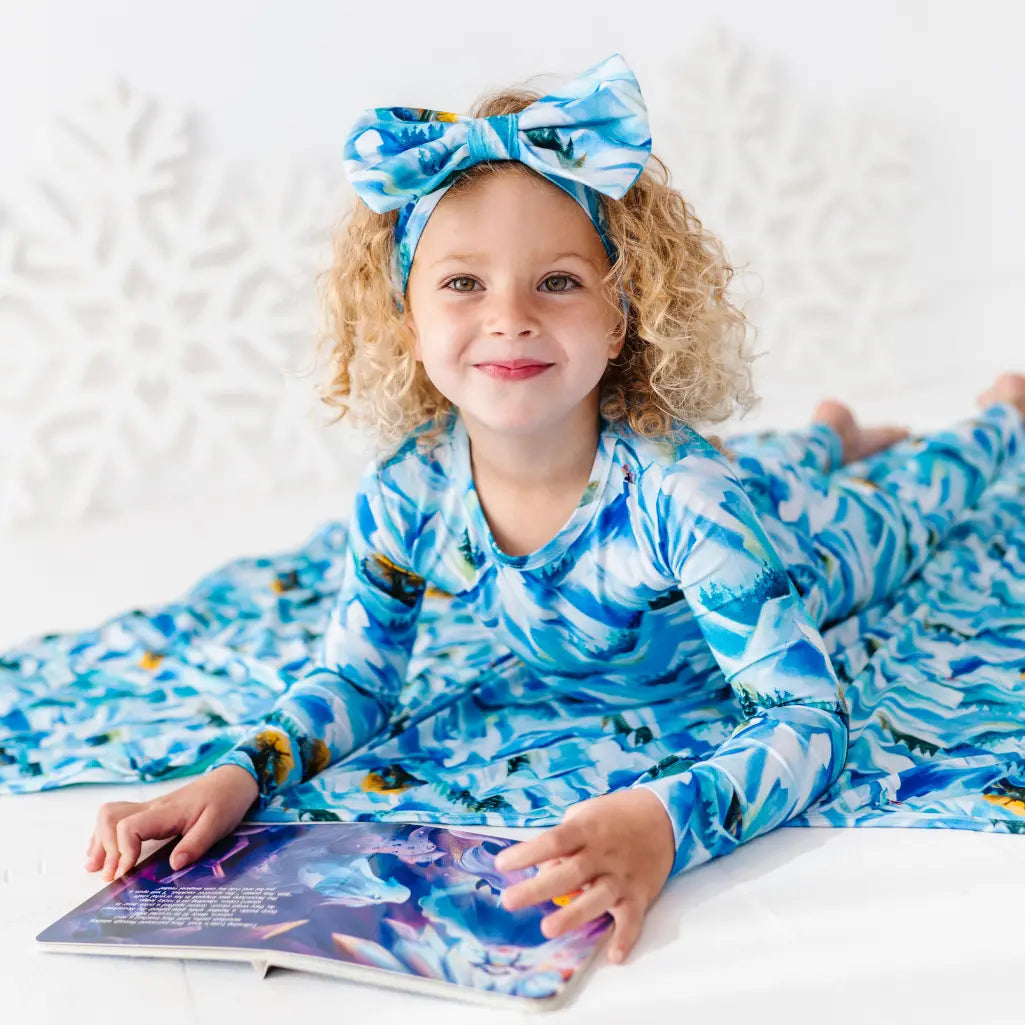Child wearing a blue and white patterned outfit with a matching headband, lying on a white surface.
