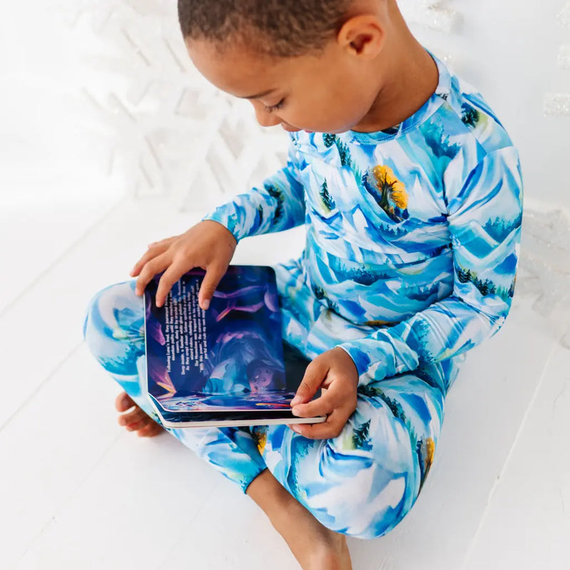 Child wearing blue and white patterned pajamas holding a tablet on a white bed.