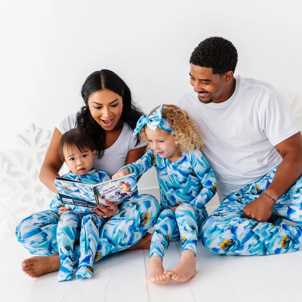 Family of four wearing matching blue and white pajamas sitting on a bed.
