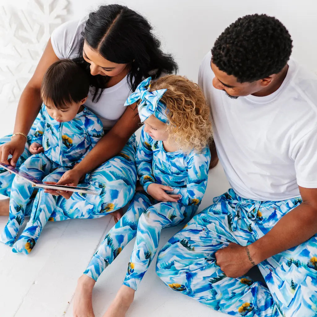 Family of four wearing matching blue and white pajamas with a pattern, sitting together on a bed.