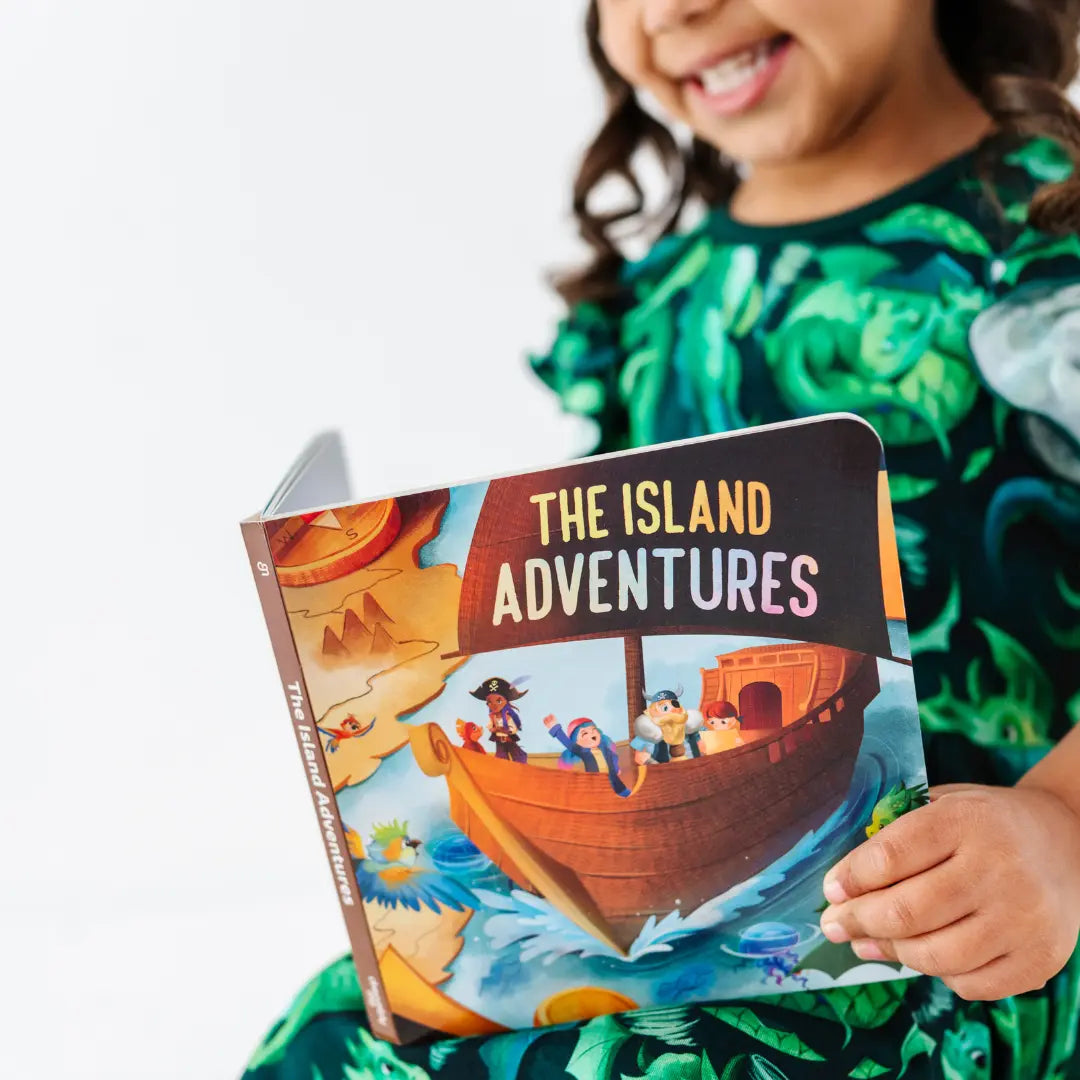 Child holding a book titled 'The Island Adventures' with a pirate-themed cover.