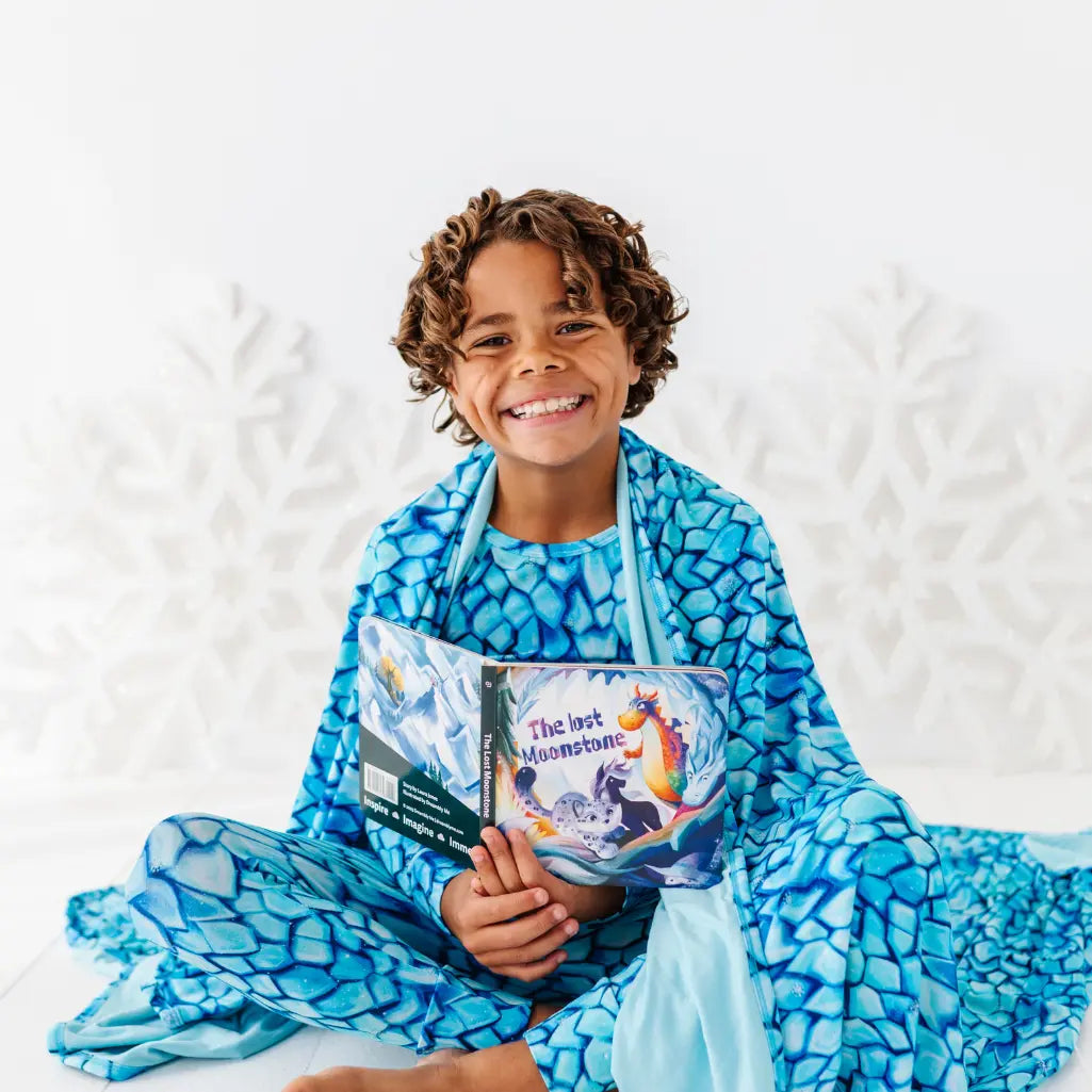 Child wrapped in a blue patterned blanket holding a book with a white background