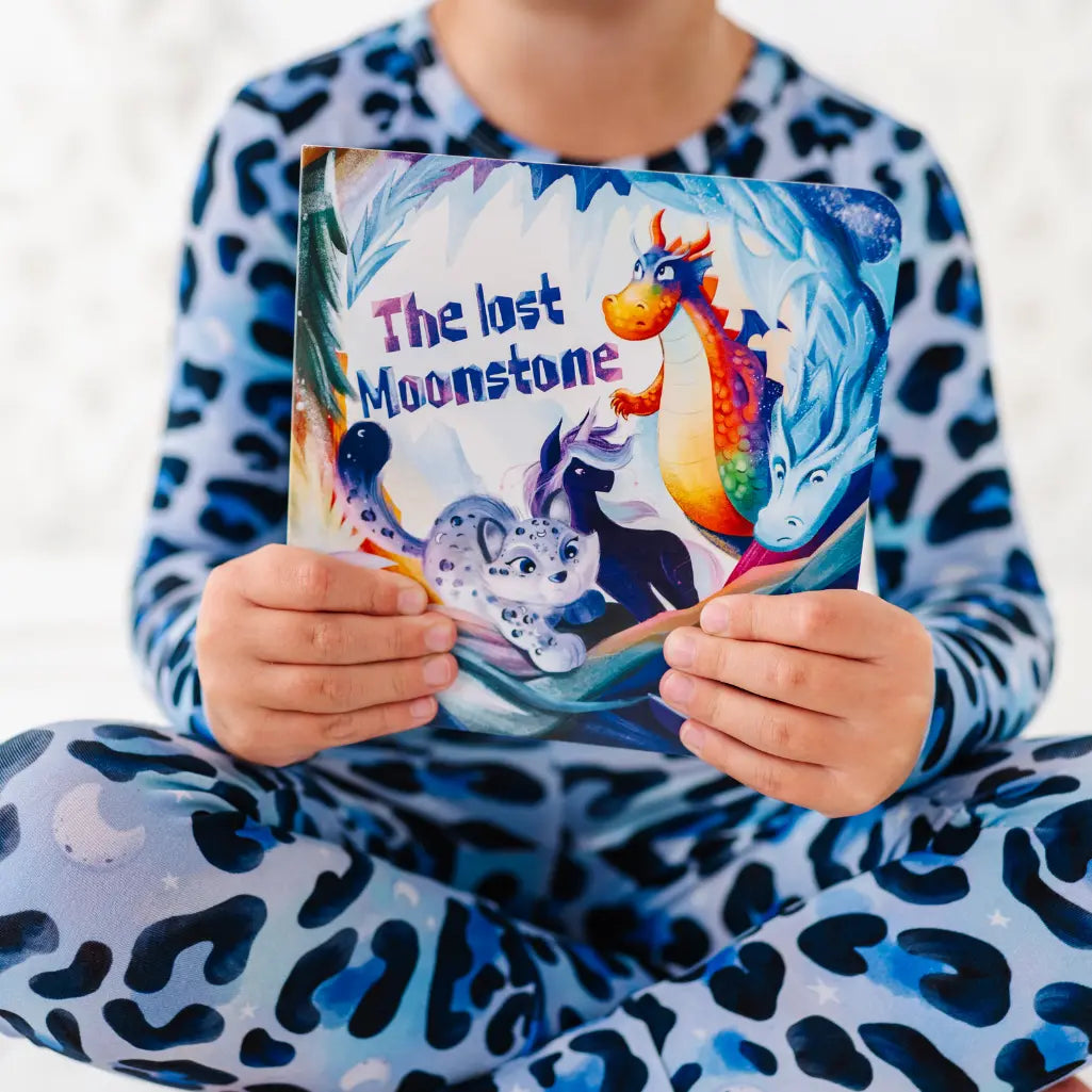 Child holding a book titled 'The Lost Moonstone' in pajama with animal print
