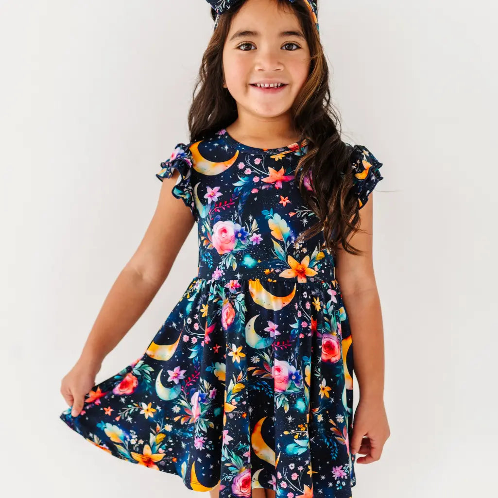 Young girl wearing a colorful dress with floral and moon designs on a white background