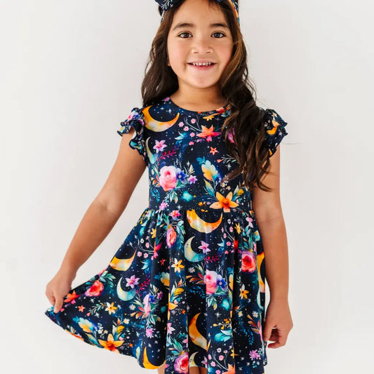 Young girl wearing a colorful dress with floral and moon designs on a white background