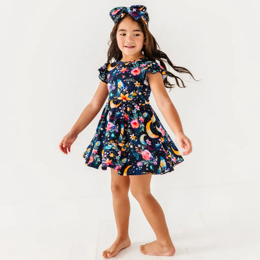 Young girl wearing a colorful dress with a space-themed pattern on a white background