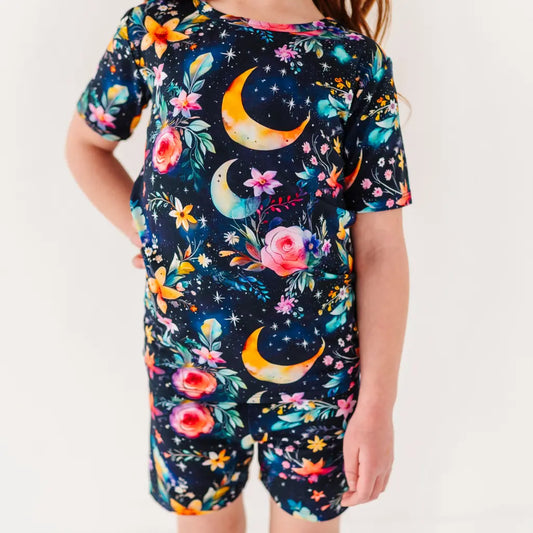 Child wearing a colorful outfit with floral and moon designs on a plain background