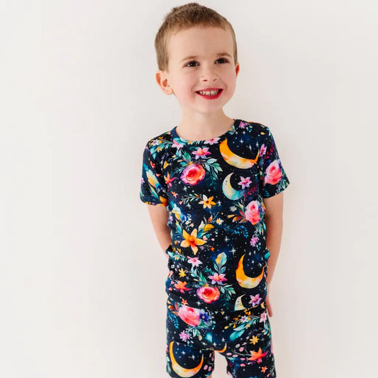 Child wearing a colorful pajama set with floral and moon designs on a plain background
