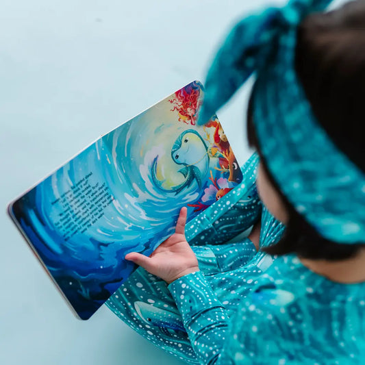 Child in teal outfit holding a colorful book with a whale illustration.