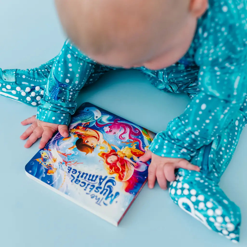 Baby in blue outfit with colorful book on light blue surface