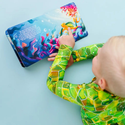Child's hand interacting with a colorful underwater-themed book on a light blue background.