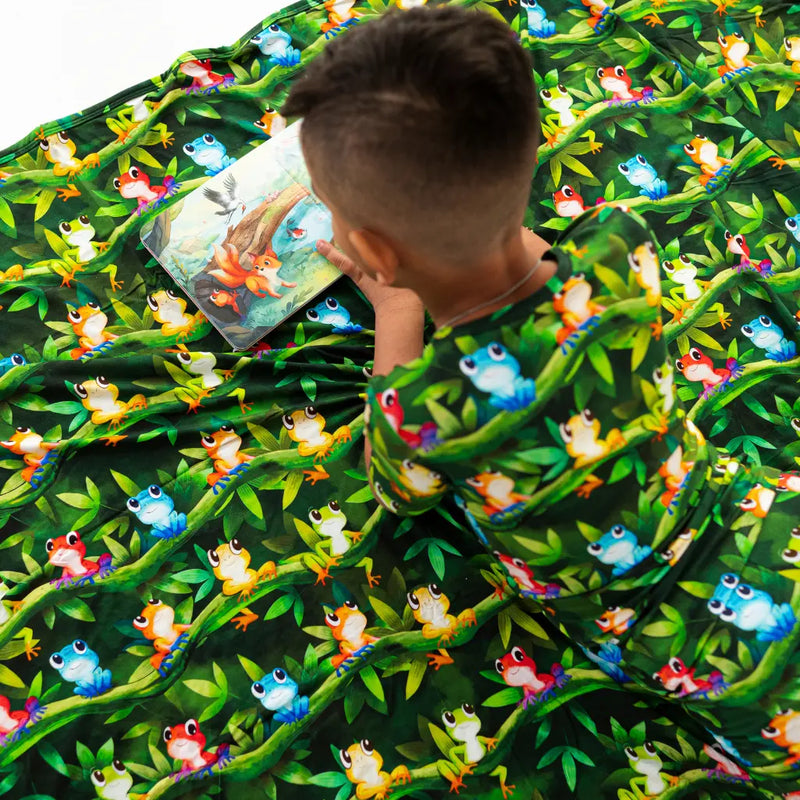 Child reading a book on a green fabric with colorful frog pattern
