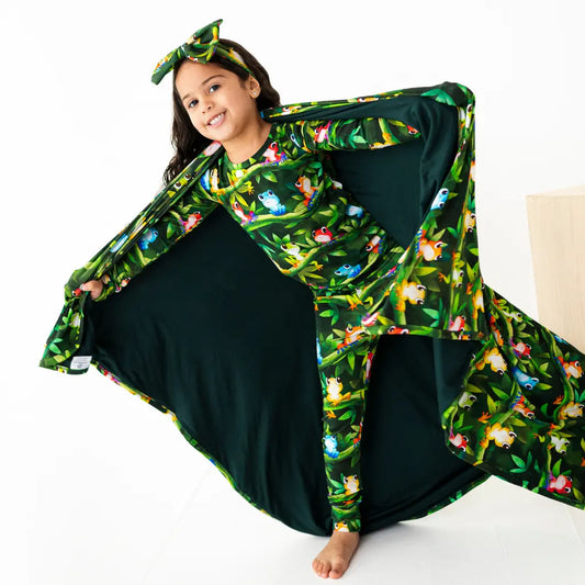 Child wearing a green floral cape with a black dress underneath on a white background