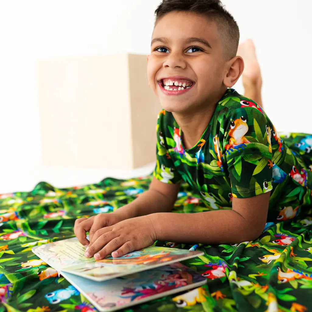 Child in a jungle-themed outfit lying on a bed with a book, surrounded by matching bedding.