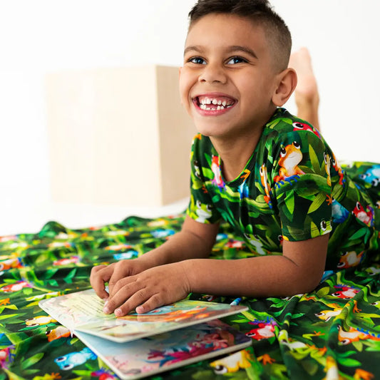 Child in a jungle-themed outfit lying on a bed with a book, surrounded by matching bedding.