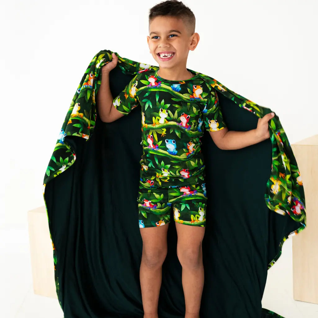 Child wearing a green animal print outfit with a matching cape, standing against a white background.