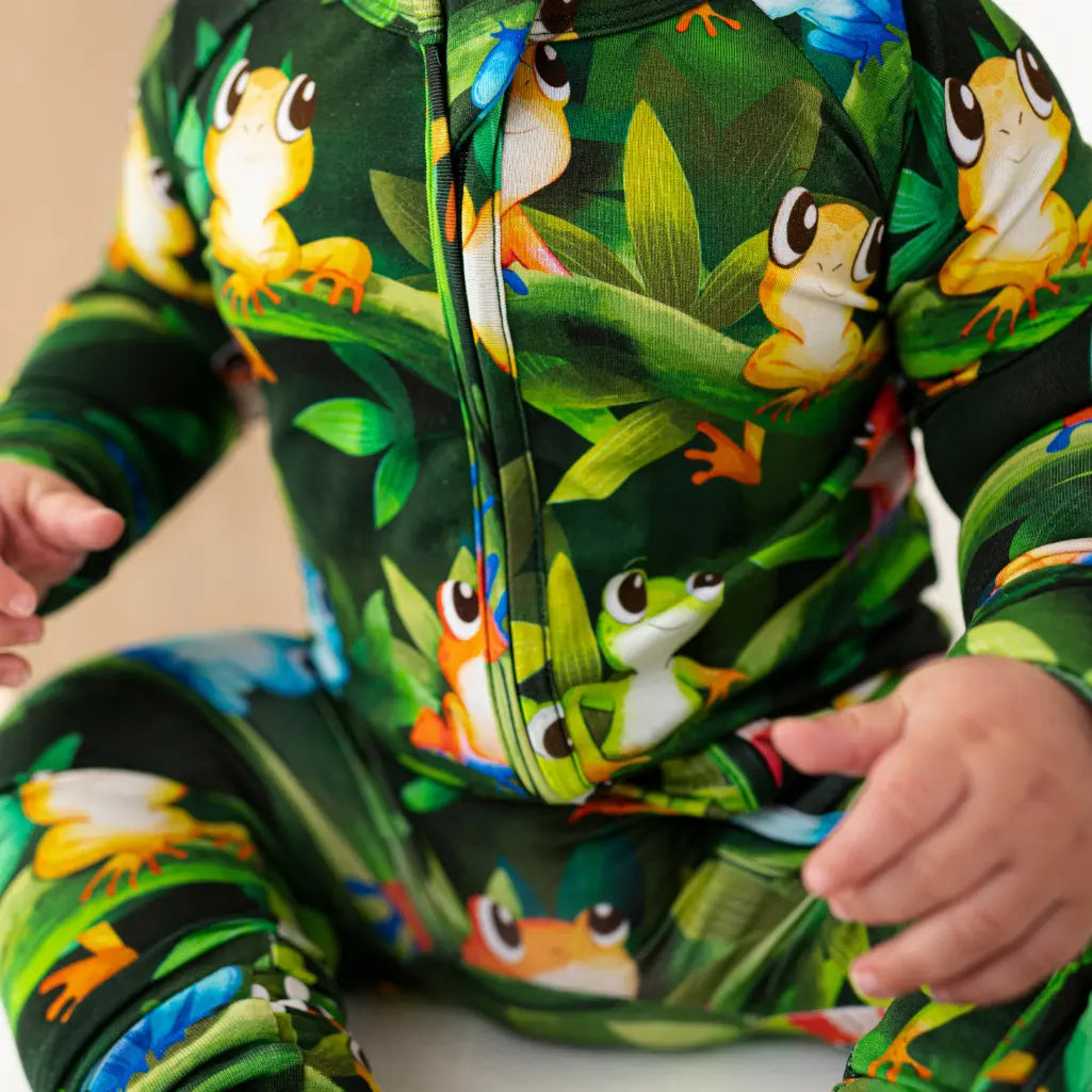 Close-up of a baby wearing a dark green onesie with colorful frog print design