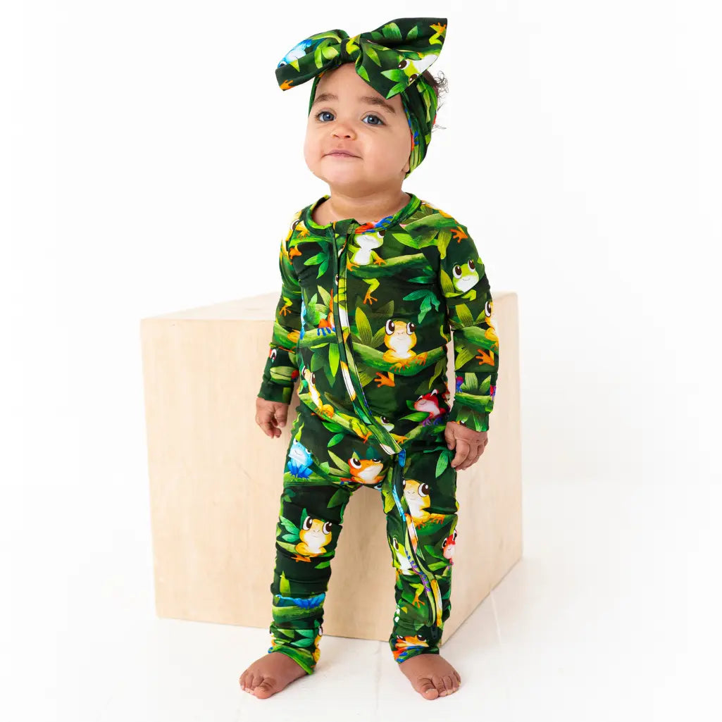 Baby wearing a green jungle-themed onesie and headband on a white background