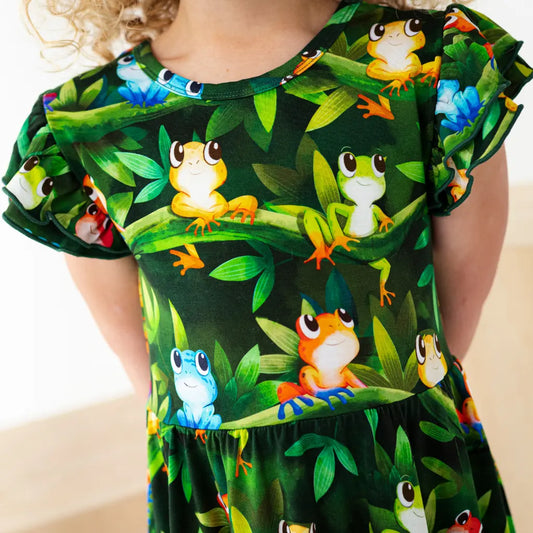 Child wearing a dress with colorful frog pattern on a plain background