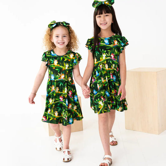 Two children wearing matching green dresses with animal prints on a white background