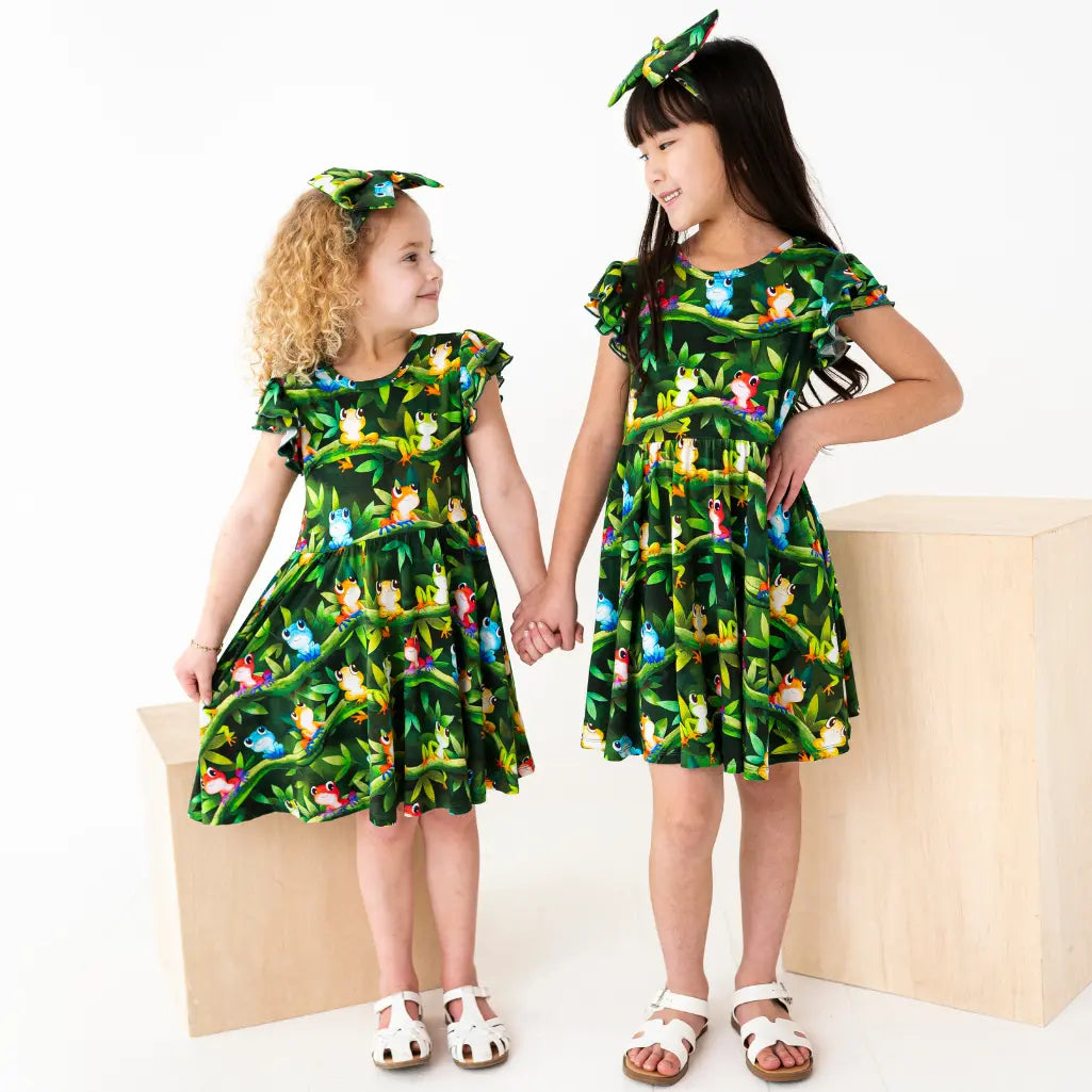 Two children wearing matching green dresses with animal prints on a white background