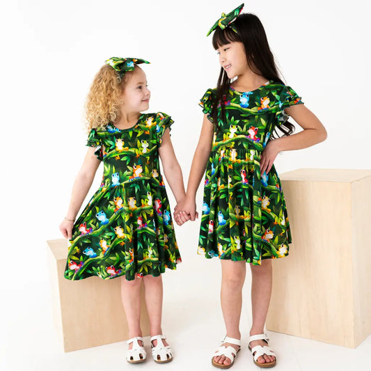 Two children wearing matching green dresses with animal prints on a white background