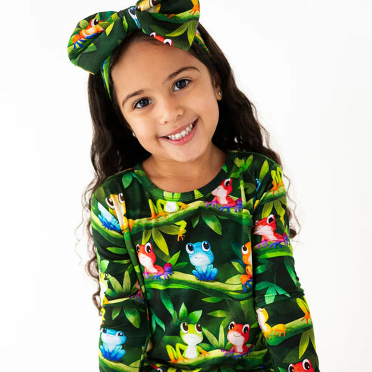 Child wearing a green long-sleeve shirt with colorful frog design and matching headband on a white background