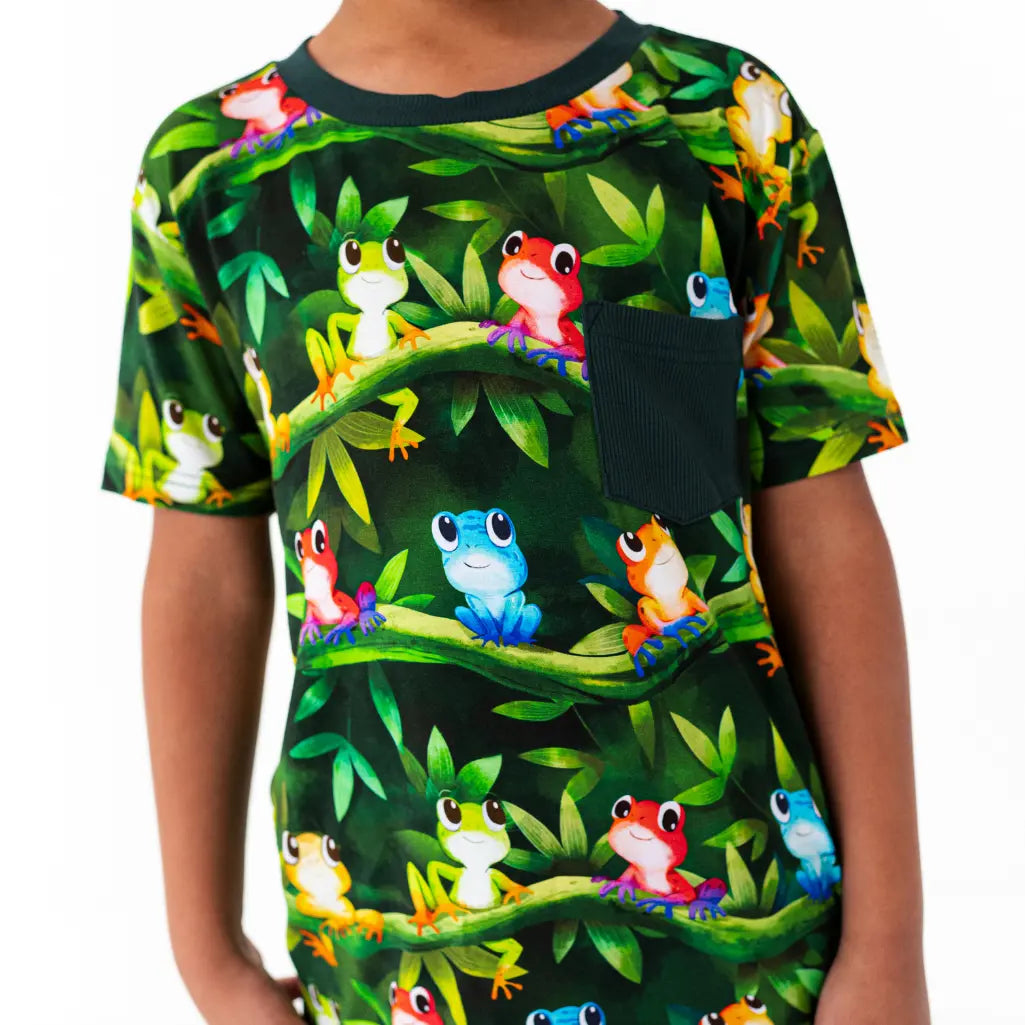 Child wearing a t-shirt with colorful frog pattern on a green background