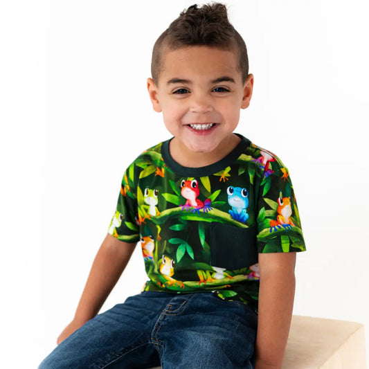 Child wearing a colorful t-shirt with cartoon frogs and plants on a white background