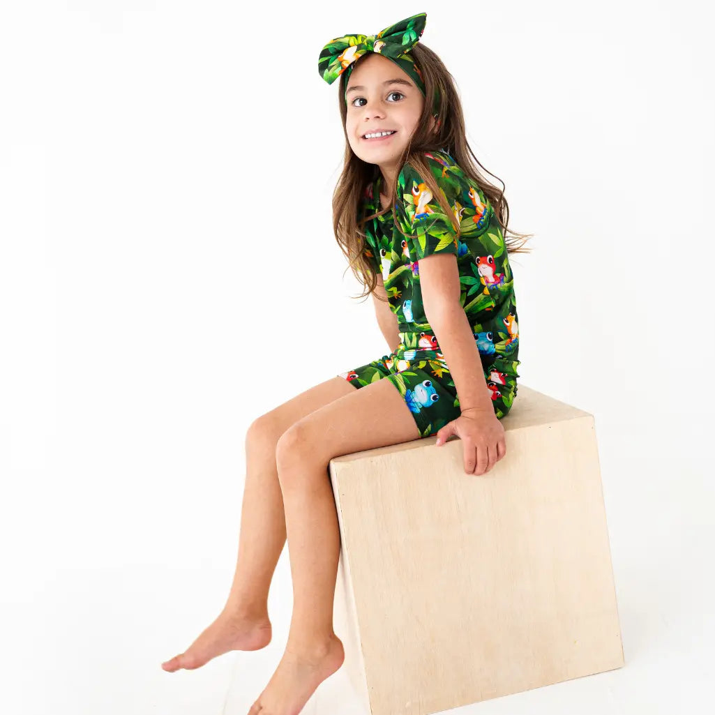 Child wearing a colorful tropical-themed outfit sitting on a block.