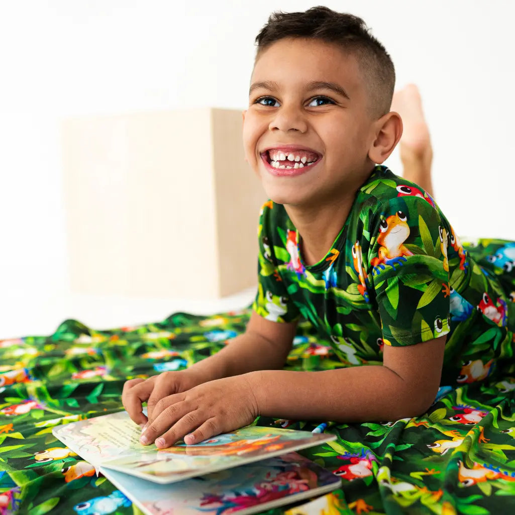 Child wearing a jungle-themed shirt and pajama set, sitting on a bed with a book.