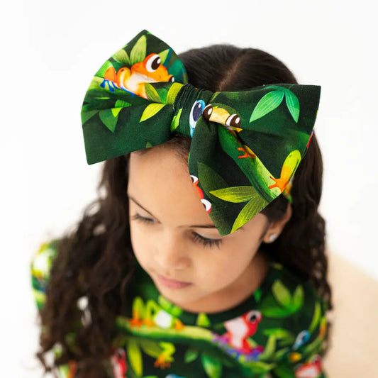 Child wearing a large green headband with frog designs on a white background