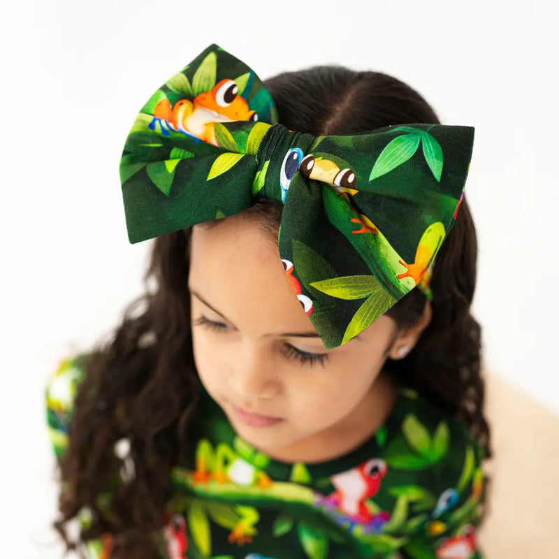 Child wearing a large green headband with frog designs on a white background