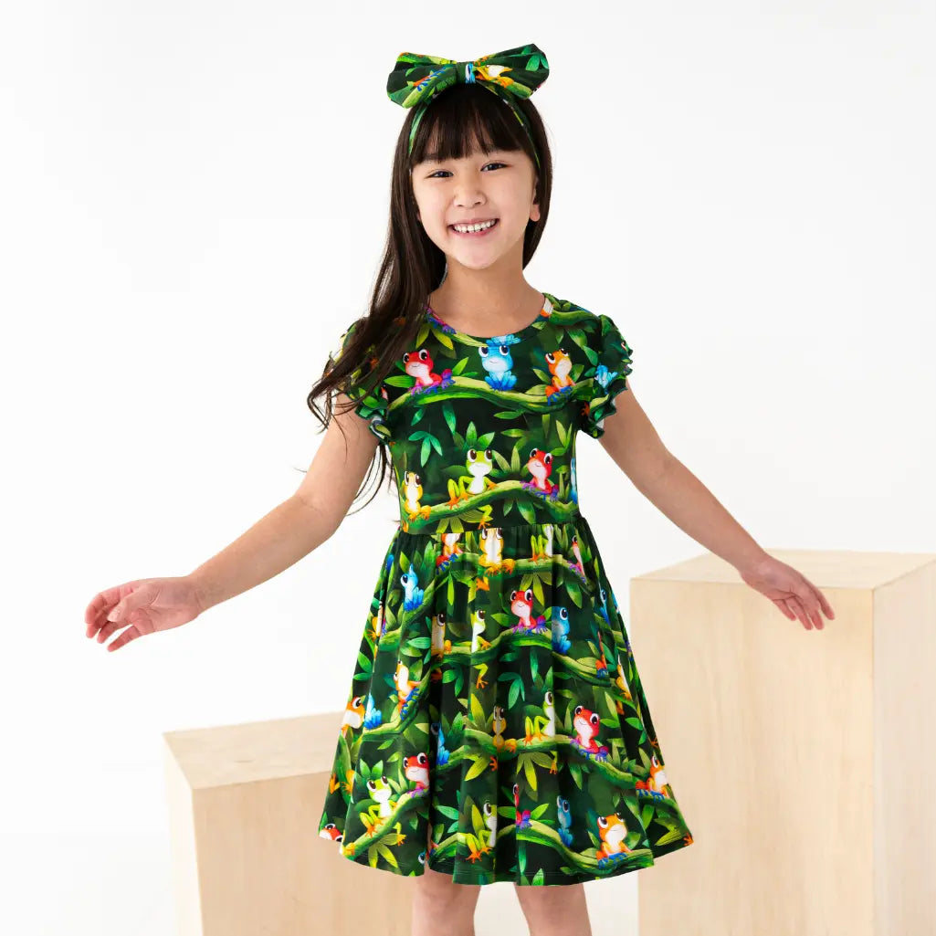 Young girl wearing a green dress with animal print and a matching headband on a white background