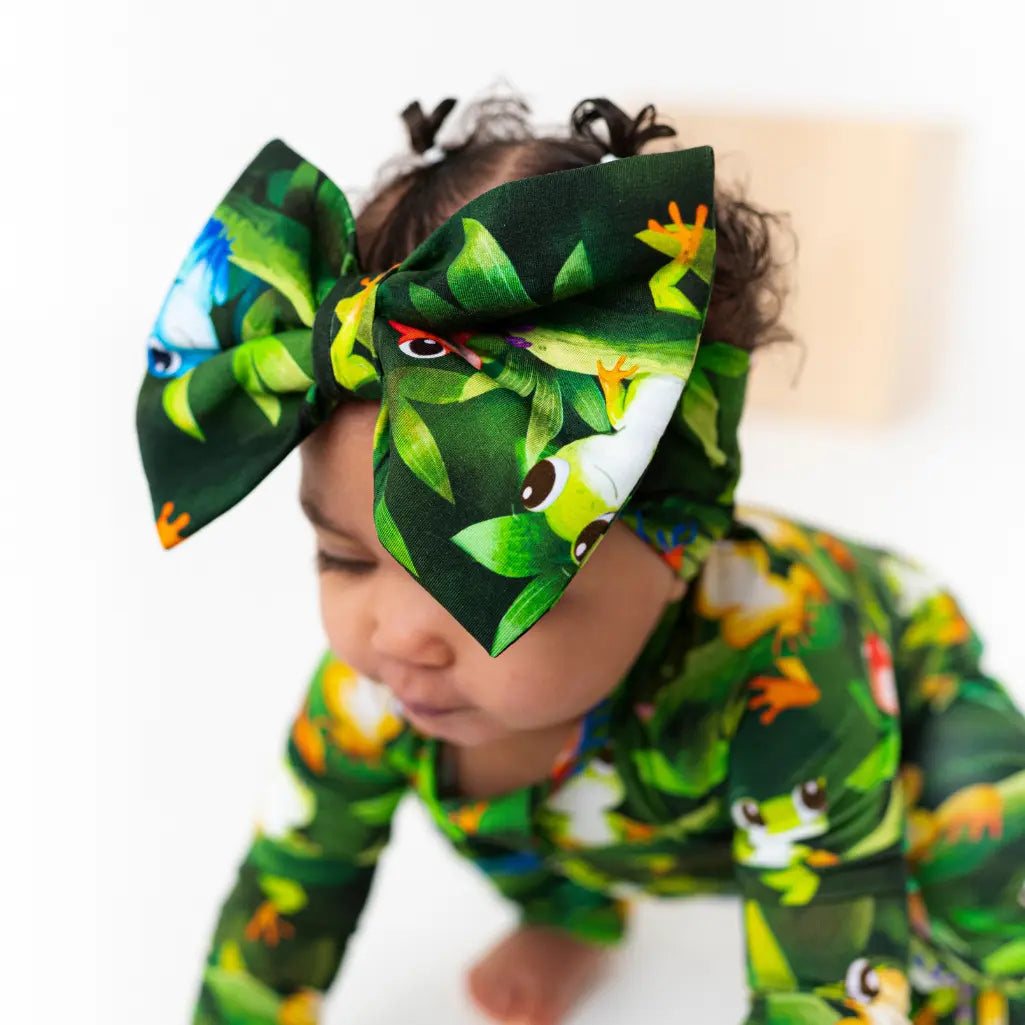 Child wearing a frog-patterned outfit and headband on a white background
