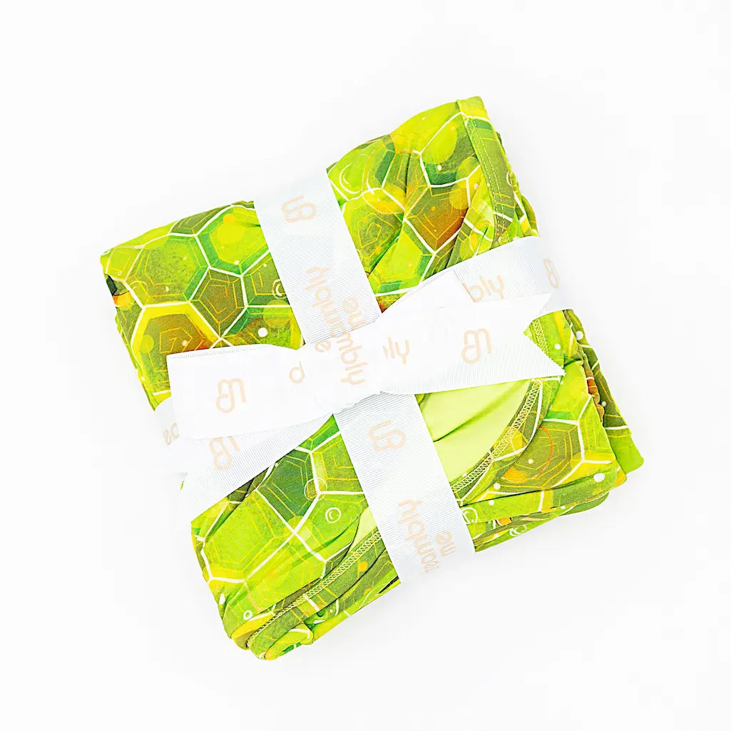 A folded green blanket with a geometric shell pattern, secured with a white tie.