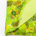 A blanket with a geometric green shell pattern and hexagonal design, featuring an image of Kai the Sea Turtle.