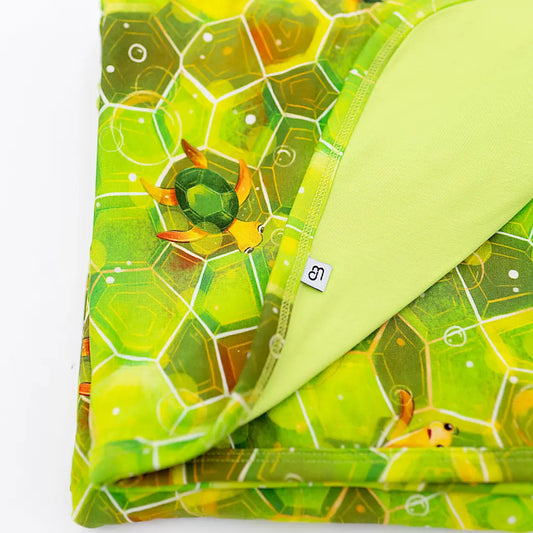 A blanket with a geometric green shell pattern and hexagonal design, featuring an image of Kai the Sea Turtle.